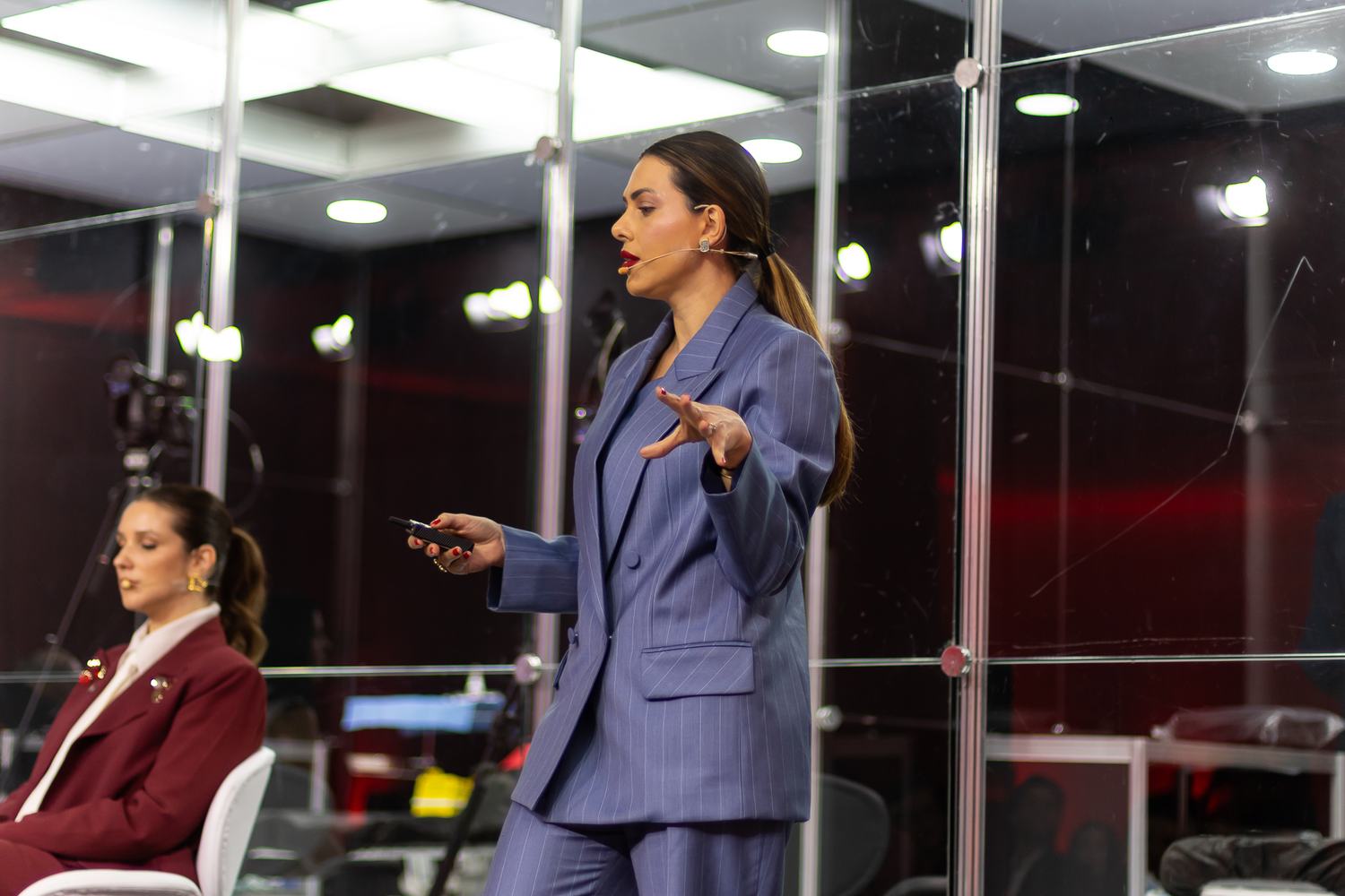 Palestrante apresenta enquanto colega acompanha sentada no palco